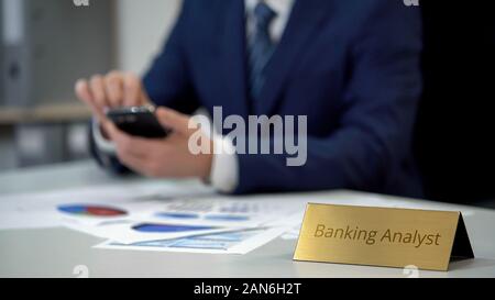 Busy male banking analyst using smartphone, checking data for financial report Stock Photo
