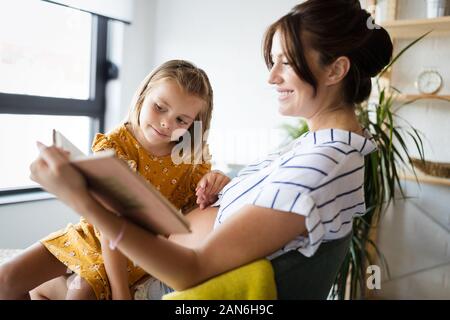 Girl and her pregnant mother reading book together. Family time Stock Photo