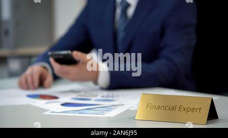 Young financial expert analyzing business documents, using mobile application Stock Photo