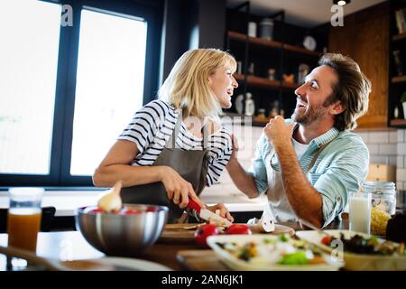 Beautiful young couple is talking and smiling while cooking healthy food in kitchen at home Stock Photo