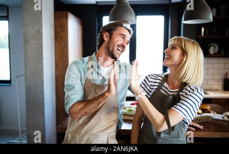 Beautiful young couple is smiling while cooking together in kitchen at home Stock Photo