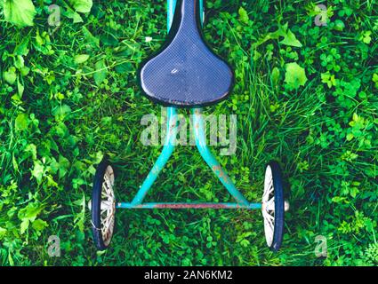 Abstract high angle view of old retro rusty children's tricycle standing on green grass