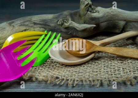 Rustic wooden utensils in a kitchen still life with two spoons and colorful plastic forks over a weathered log of wood on hessian Stock Photo