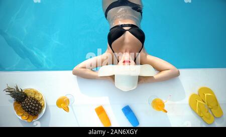 Attractive woman in bikini and hat relaxing in swimming pool, summer resort Stock Photo