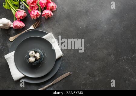 Easter table setting with quail eggs in nest and pink tulip on dark. Top view. Easter dinner. Top view. Stock Photo