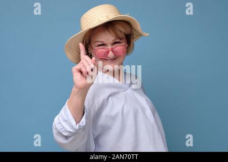 I got excellent advice for daughter. Excited and enthusiastic creative senior woman in summer hat and pink glasses raising index finger in eureka gest Stock Photo
