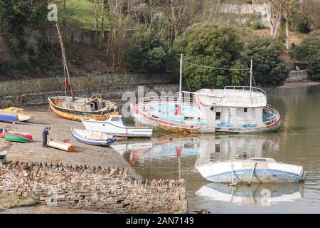 CONWY, UK - February 26, 2012. An elderly man repairs a dinghy (small boat) on the shore at Conwy, Wales Stock Photo