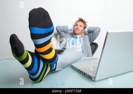 Thoughtful businessman relaxing with his socks up on the desk next to his laptop computer Stock Photo