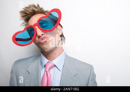 Man wearing suit with pink tie giving a big smooch to the camera behind a pair of crazy oversized heart-shaped sunglasses Stock Photo