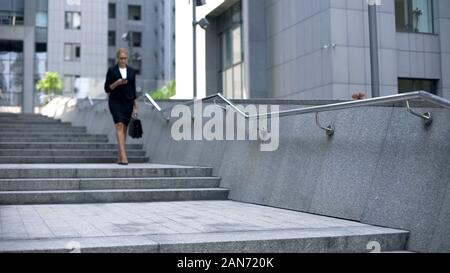 Beautiful woman walking down stairs and checking mail on smartphone, busy life Stock Photo