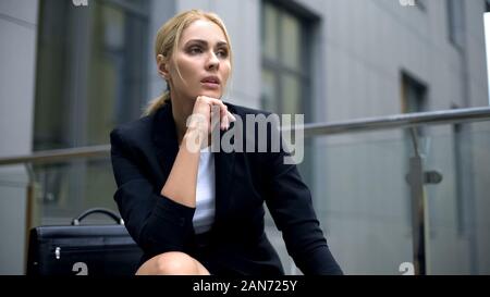 Thoughtful blond businesswoman sitting on bench, problems or stress at work Stock Photo