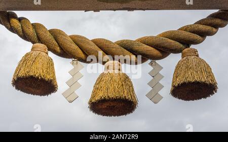 Sacred rope, or shimenawa, and zigzag streamers, or shide, on torii gate to small local shinto shrine, Kumagawa, Japan. Stock Photo