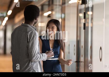 Smiling millennial multiracial colleagues talk in office hallway Stock Photo