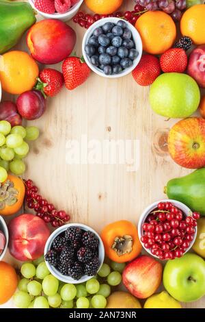 Rainbow fruits berries background circle frame, uncut and whole on light pine wood table, flat lay, copy space for text, selective focus Stock Photo