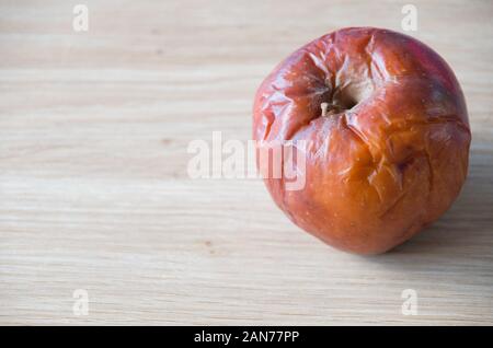 Old rotten apple isolated on a wooden bench top covered in wrinkles and bruises Stock Photo
