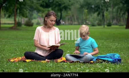 Mom reading book, son using tablet, alternative education with IT technologies Stock Photo
