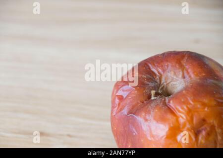 Old rotten apple isolated on a wooden bench top covered in wrinkles and bruises Stock Photo