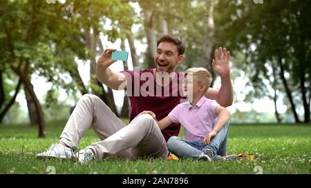 Father and son talking with mother via smartphone, video conference outdoors Stock Photo