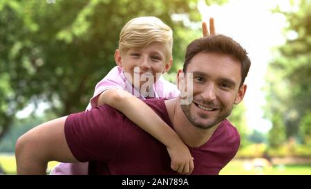 Son and father posing on camera, enjoying piggyback ride, fooling around, fun Stock Photo