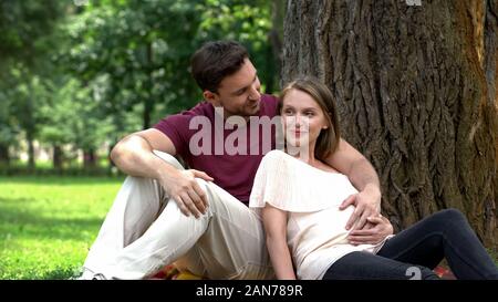 Happy pregnant couple sitting in park, planning secured family life, welfare Stock Photo