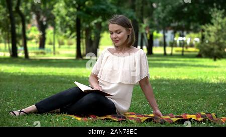 Calm pretty woman reading book about self-development in park, leisure time Stock Photo