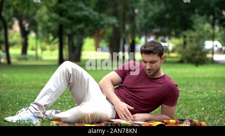 Concentrated male reading book in central park, laying on plaid, free time Stock Photo