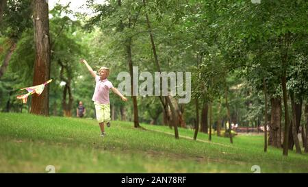 Happy boy launching kite in park, leisure activity outdoors, carefree childhood Stock Photo