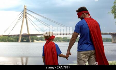 Dad and son in superhero costumes holding hands, father protection and support Stock Photo