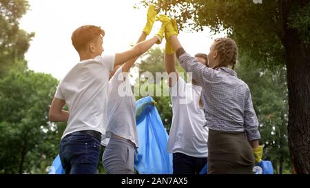 Team of volunteers hi-fiving during collecting garbage in park, save nature Stock Photo