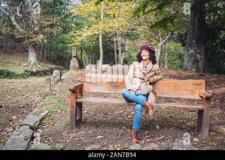 White woman in vintage style wear sitting on a wooden bench outdoors Stock Photo