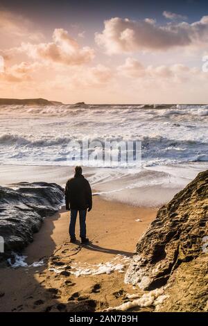 A man standing alone on the beach and watching the incoming waves in a choppy sea at Little Fistral in Newquay in Cornwall. Stock Photo