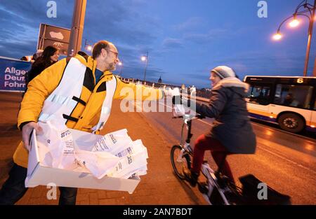 Mainz, Germany. 16th Jan, 2020. Michael, ADFC Ortsgruppe Wiesbaden, hands over a Kreppel to a cyclist. The German Cycling Club (ADFC) distributes crepe and apples to cyclists on the closed Theodor-Heuss-Bridge. The local groups of the cycling clubs of Mainz and Wiesbaden would like to thank the commuters who switched to their bikes during the closure due to renovation work. Credit: Andreas Arnold/dpa/Alamy Live News Stock Photo