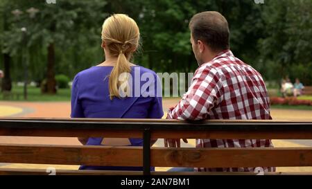 Back view of couple sitting on park bench, spending time together, conversation Stock Photo