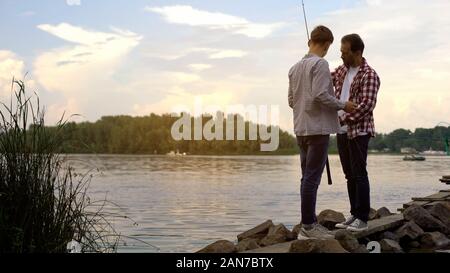 Father and 16 years old son preparing fishing rods, relaxing together near lake Stock Photo
