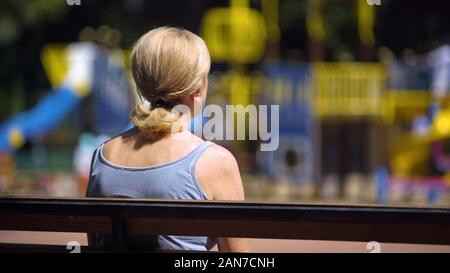 Sad old female sitting on playground bench and looking at children, infertility Stock Photo