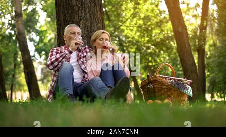 Senior couple sitting on grass and drinking wine, romantic date, anniversary Stock Photo