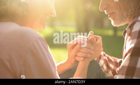 Smiling retired couple relaxing in park, holding hands and talking about love Stock Photo