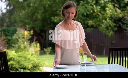 Pretty housewife serving table, waiting kids and husband for dinner outdoors Stock Photo