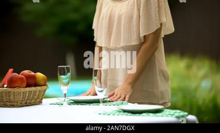 Wife serving table for two, romantic dinner outdoors, preparing for date Stock Photo