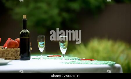Wine bottle and two glasses on table in summer garden, preparations for dinner Stock Photo