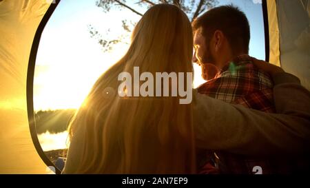 Lovers admiring sunset from tent on the beach, camping in wild, happy moments Stock Photo