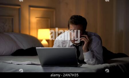 Thoughtful male typing on laptop and talking on phone preparing report, deadline Stock Photo