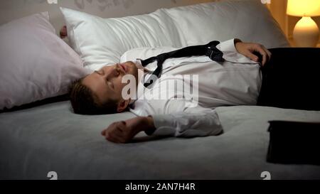 Drunk man in business suit sleeping in hotel room, suffering alcoholism, party Stock Photo