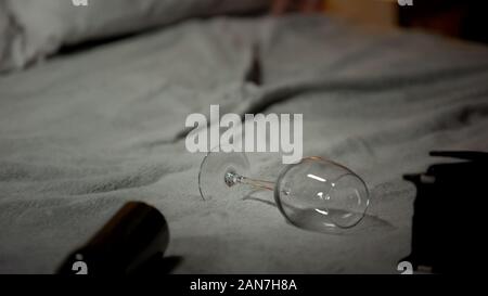 Empty wine glass and bottle lying on bed, alcohol abuse concept, alcoholism Stock Photo