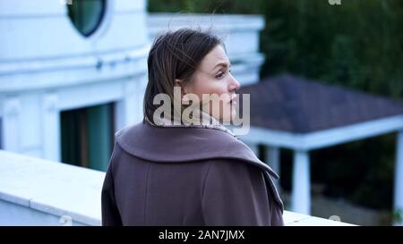 Pensive middle-aged woman standing on balcony of estate, feeling sad and lonely Stock Photo