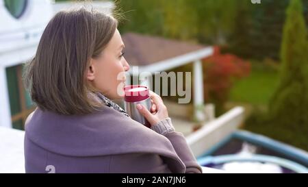 Pensive woman standing on balcony with cup of coffee, warming up on cold day Stock Photo