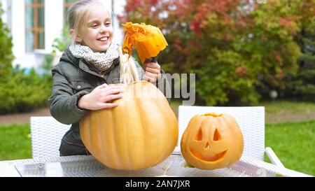 Nice smiling girl carving pumpkin Jack, having fun, enjoying Halloween eve Stock Photo