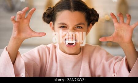 Little vampire girl with big fangs making scary faces at All Hallows Eve party Stock Photo