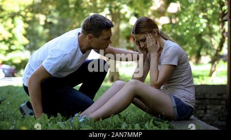 Girl suffering from migraine, sitting in park, man calling ambulance, first aid Stock Photo
