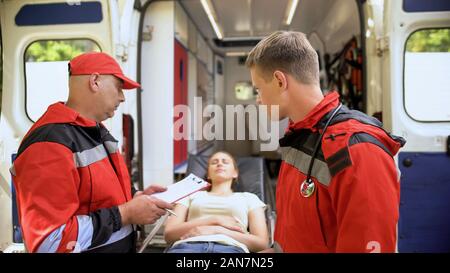 Male paramedics examining patient on stretcher, making records, rescue team Stock Photo